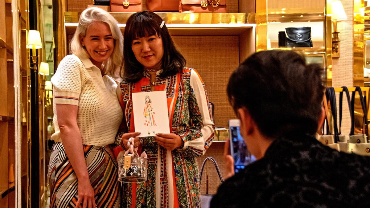 A Chinese shopper poses for a photo with her miniature portrait created by Tory Burch's artist at the store's VIP cocktail event.