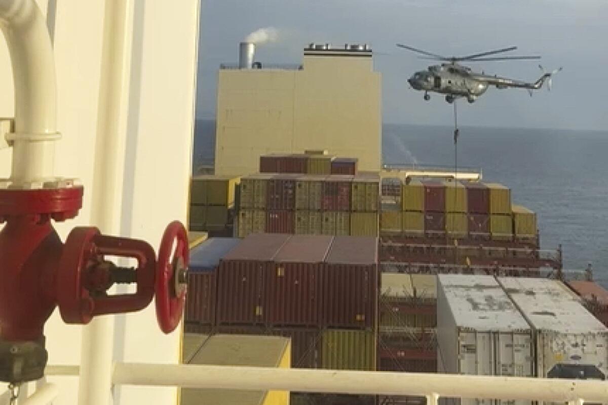 A person rappels on a line from a helicopter onto a container ship. 