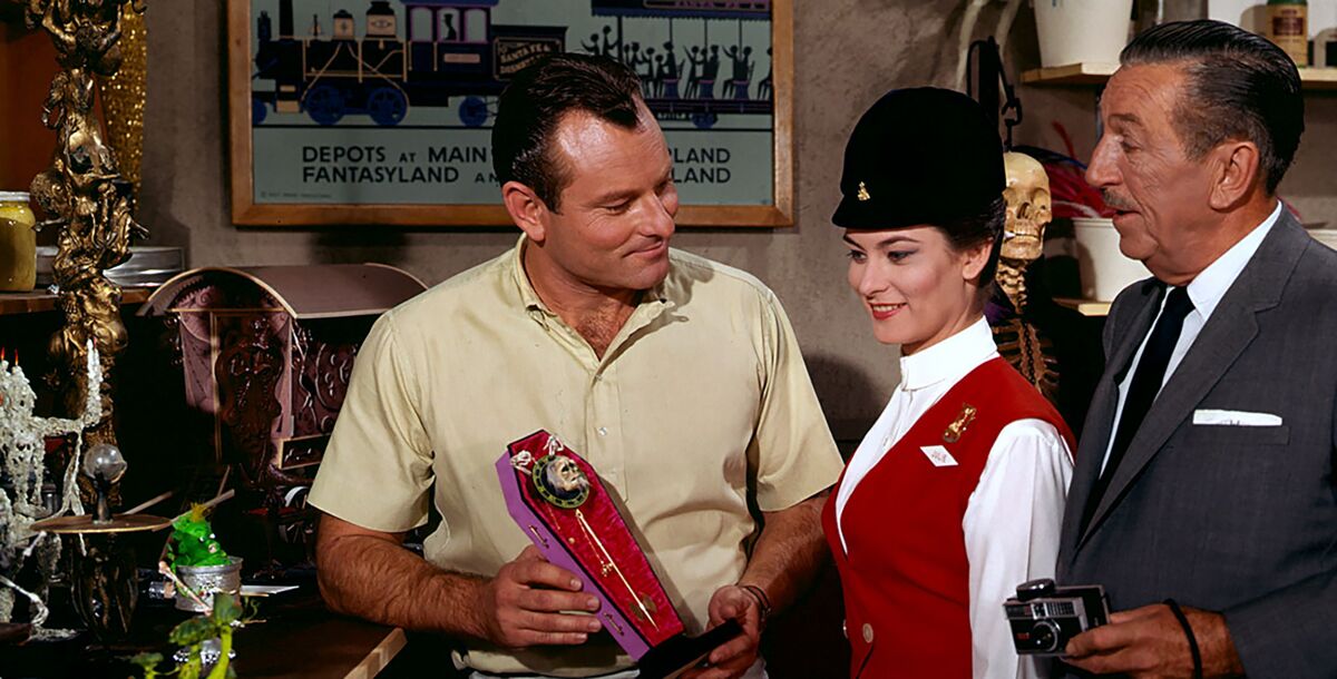 Rolly Crump and Walt Disney stand amid theme park models.