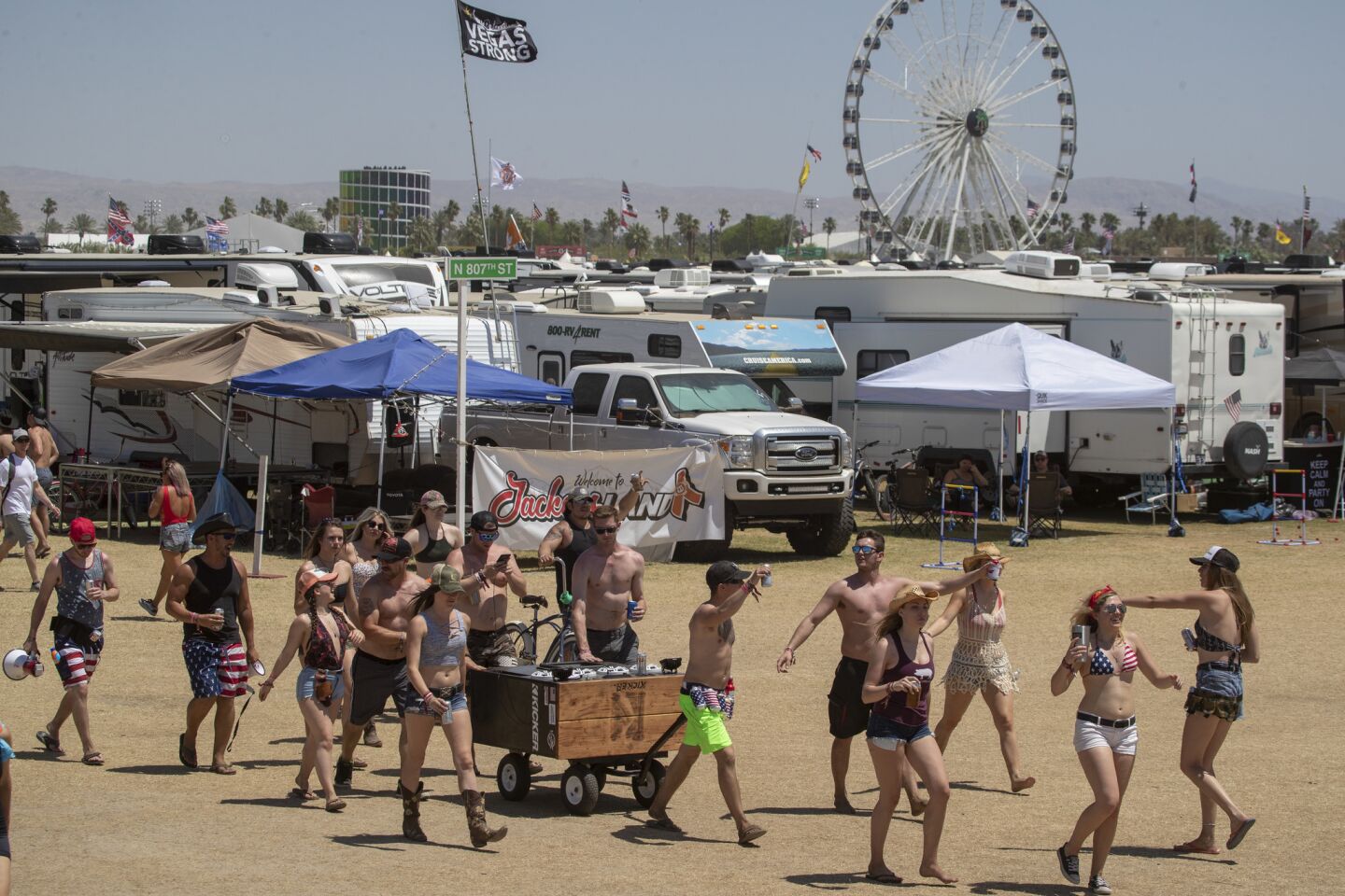 Country music fans parade through the RV area at the Empire Polo Club on Sunday, pulling a wagon with a giant speaker blasting music.