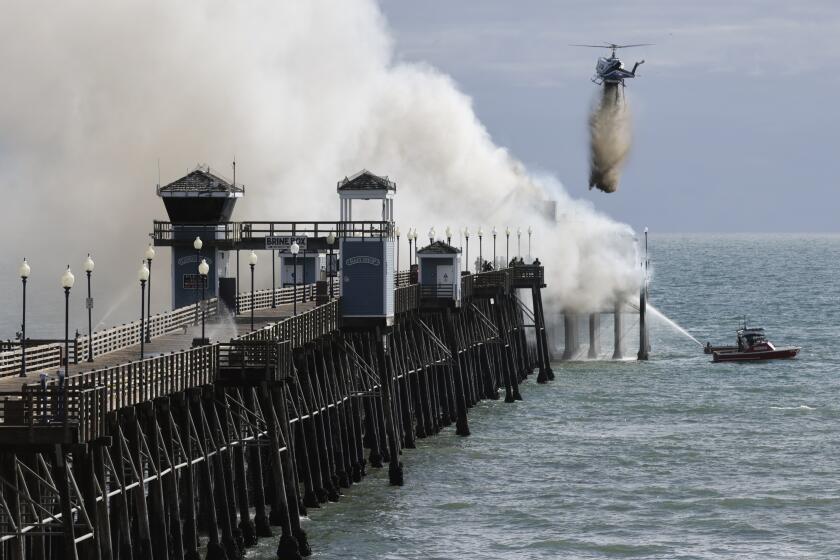 A helicopter drops water as fire crews fight a fire burning at the end of the Oceanside Municipal Pier.
