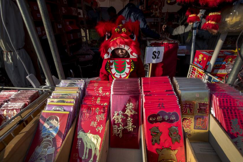 Westminster, CA - February 10: Midori Nguyen, 5, of Westminster, wears a dragon dance costume while looking over li xi, or red envelopes where a monetary gift is given during holidays, on display in preparation for the Lunar New Year at the Asian Garden Mall in Little Saigon, Westminster Wednesday, Feb. 10, 2021. For those who celebrate Lunar New Year, which starts Friday, Feb. 12, COVID has forced them to avoid touching cash and stuff traditional red envelopes normally filled with "lucky" money instead with checks, Lotto tickets, gift cards and the like. It will be the Year of the Ox. People flocked to Little Saigon to purchase holiday wares, traditional Vietnamese outfits, baked goods or flowers set up at store entrances or along the sidewalk.(Allen J. Schaben / Los Angeles Times)