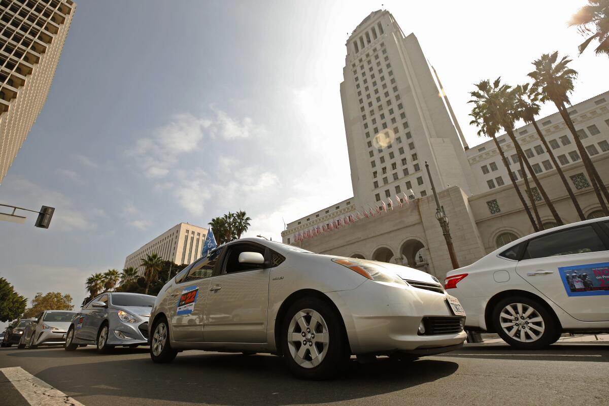 Cars with Prop 22 signage drive on road in front of Los Angeles City Hall