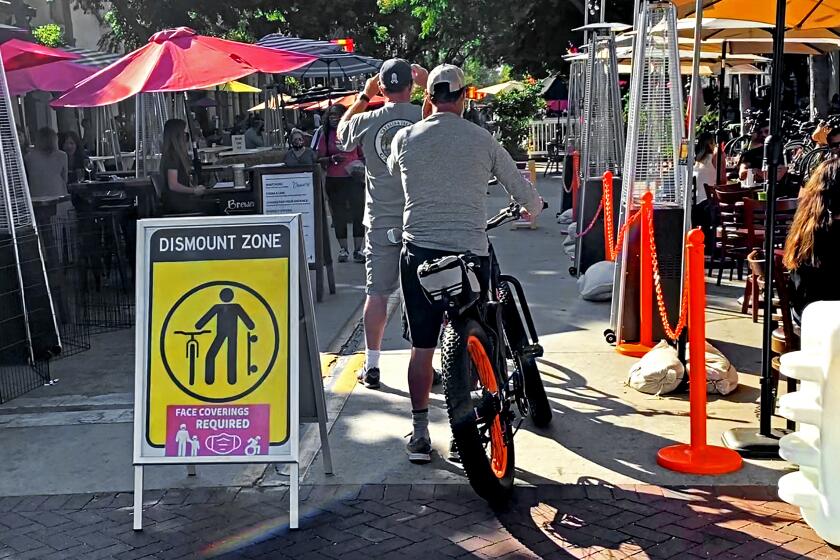 Pedestrians and cyclists share a pathway between outdoor dining areas on State Street in Santa Barbara, Calif., July, 2020.
