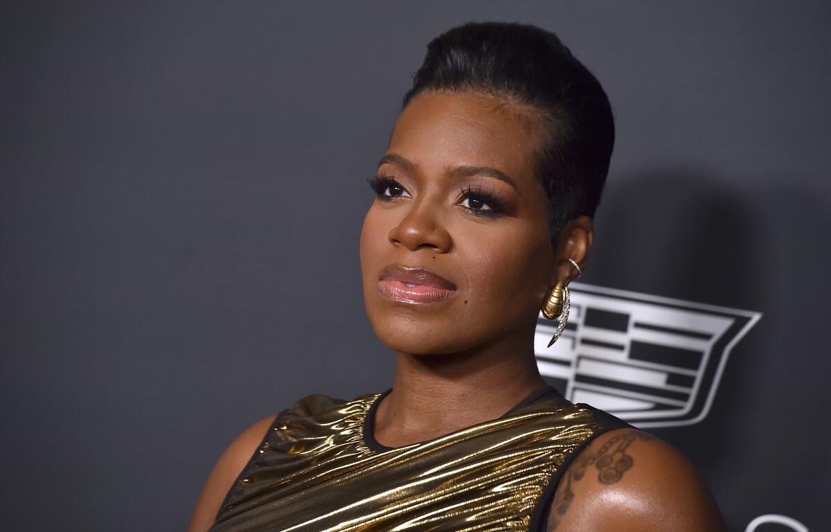 Fantasia Barrino wears a ruched bronze gown and gold dangly earrings with a slicked-back hairstyle. 