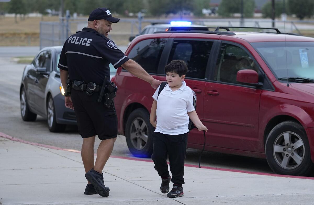 A police officer pats the back of a young boy carrying a backpack near a car.