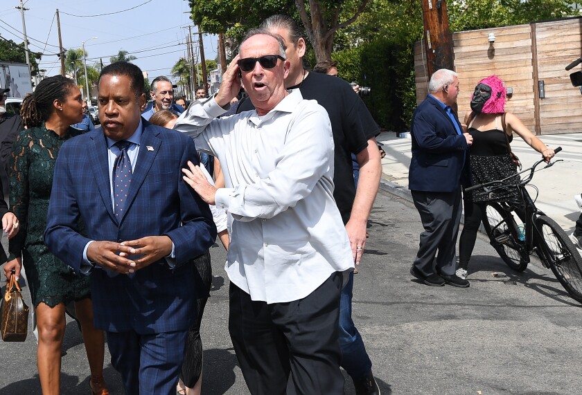 Larry Elder is escorted by a security guard after the woman in the gorilla mask, at right, threw an egg at him.
