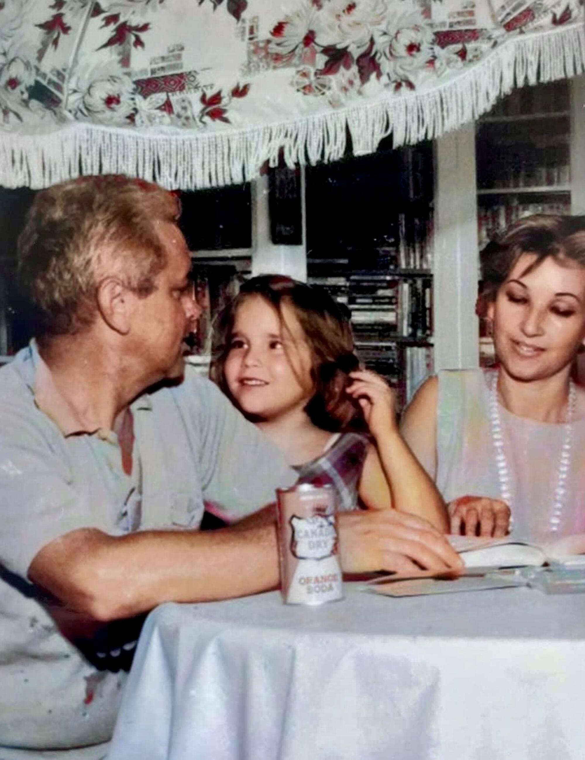 A young girl sitting at a table between her parents.