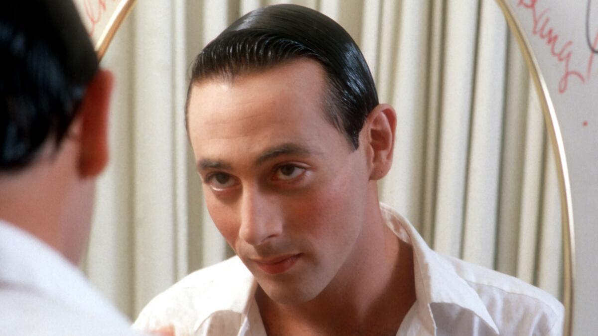 A man in a shirt looks at a reflection of himself in a mirror.