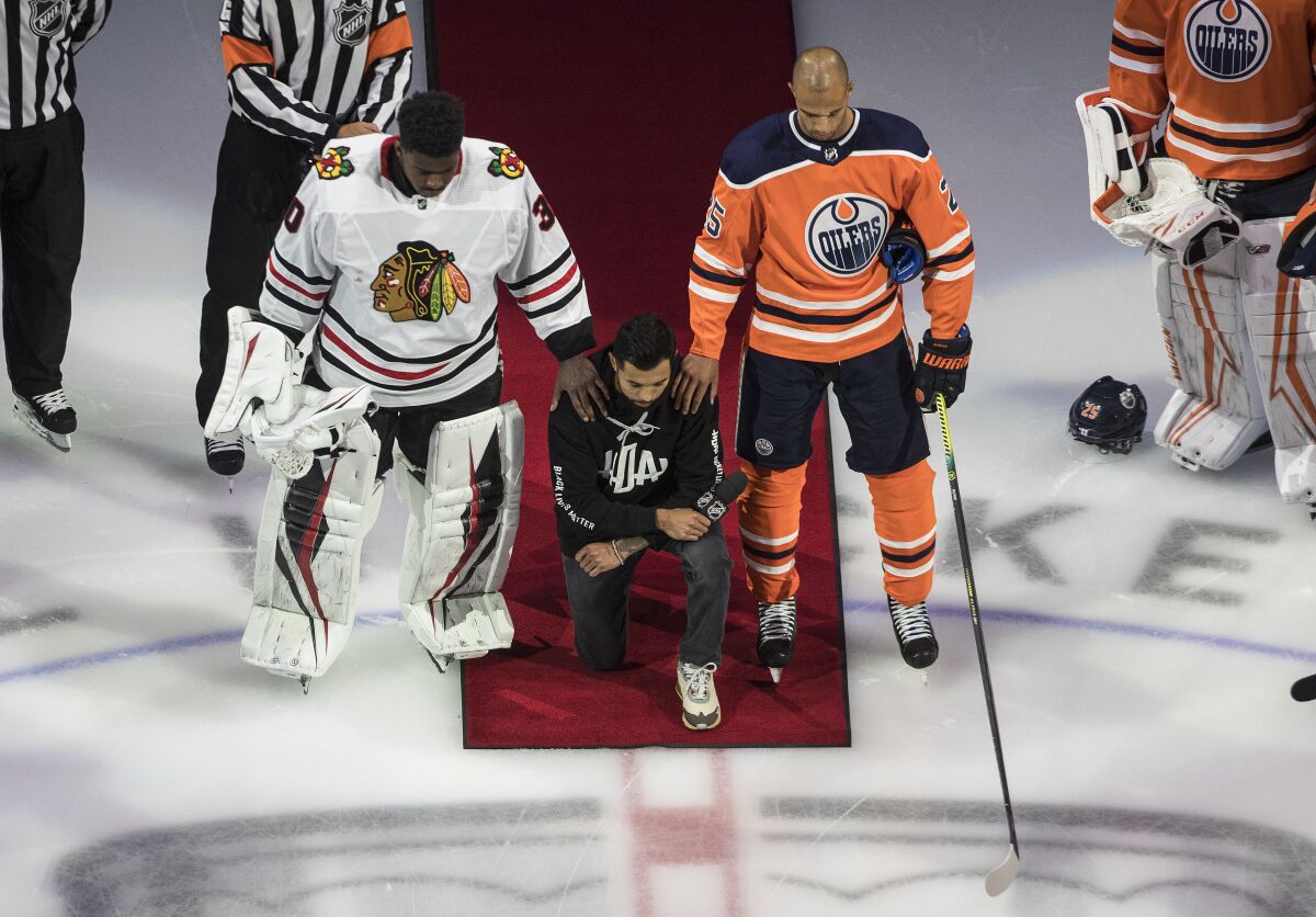 Matt Dumba takes a knee during the U.S. national anthem flanked by Oilers' Darnell Nurse and Blackhawks' Malcolm Subban