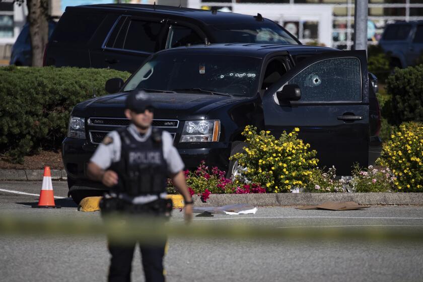 A police officer standing near a windshield and passenger window of an RCMP vehicle with bullet holes at the scene of a shooting in Langley, British Columbia, Monday, July 25, 2022. (Darryl Dyck/The Canadian Press via AP)