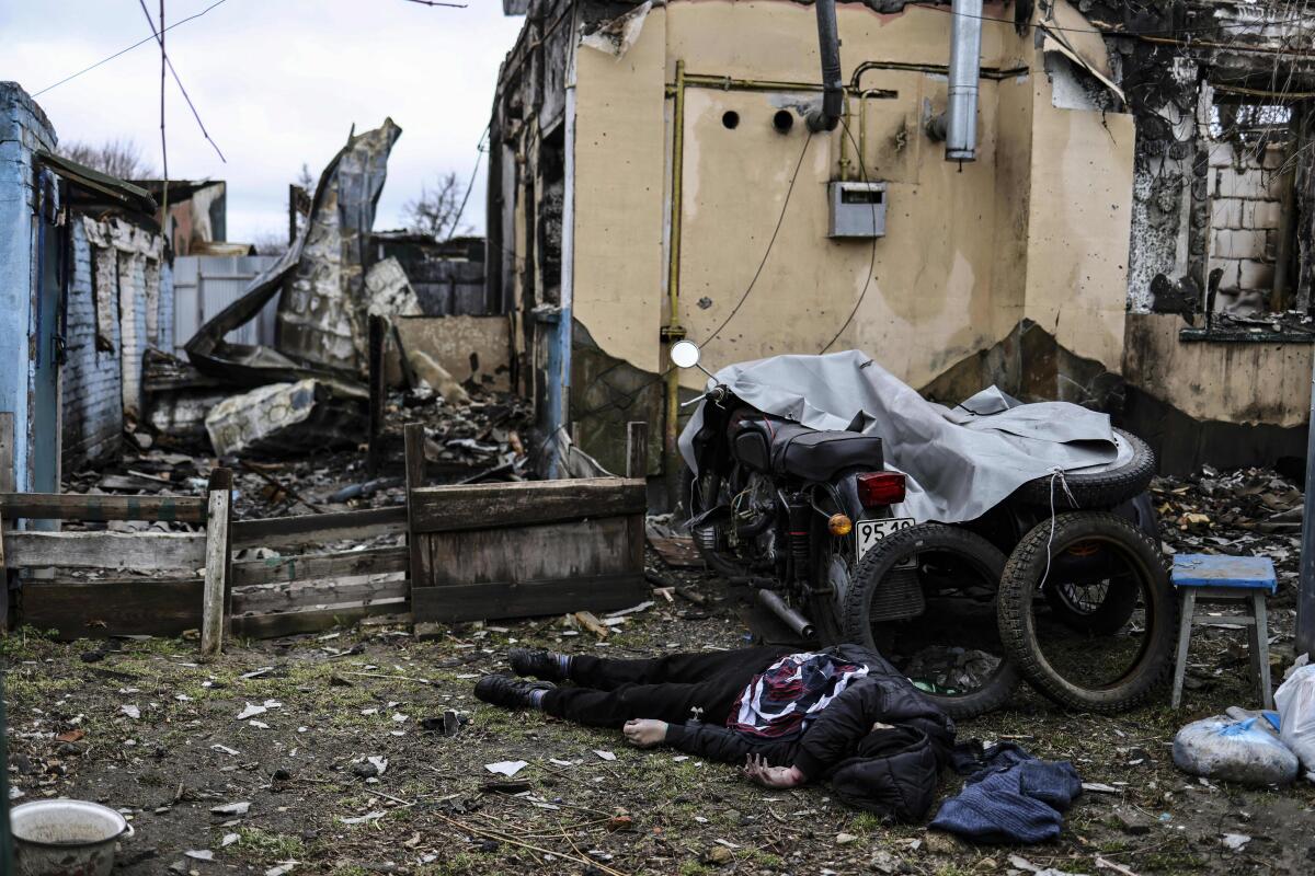 A body in dark clothing lies on the ground near a partially covered motorcycle and tires amid rubble
