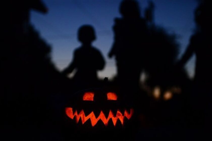 Children play behind a pumpkin carved and lit for Halloween in Monterey Park.