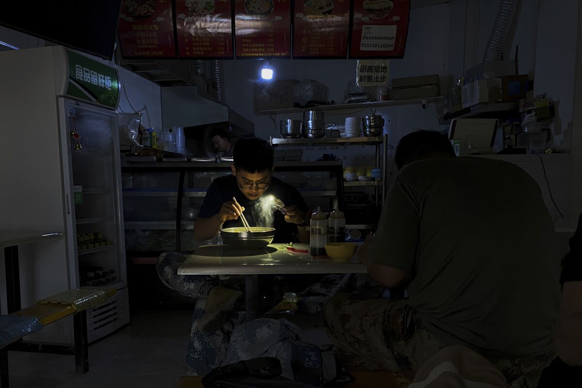 A man uses his smartphone flashlight to illuminate his bowl of noodles.