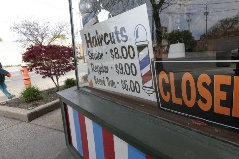 FILE - In this May 6, 2020 file photo, a woman walks past a closed barber shop in Cleveland. Small businesses are in limbo again as the coronavirus outbreak rages and the government’s $659 billion relief program draws to a close. Companies still struggling with sharply reduced revenue are wondering if Congress will give them a second chance at the Paycheck Protection Program, which ends Friday, Aug. 7, after giving out 5.1 million loans worth $523 billion. (AP Photo/Tony Dejak, File)