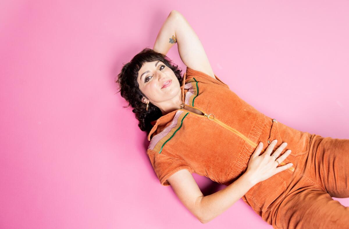 Woman in an orange jumpsuit laying down on a pink background