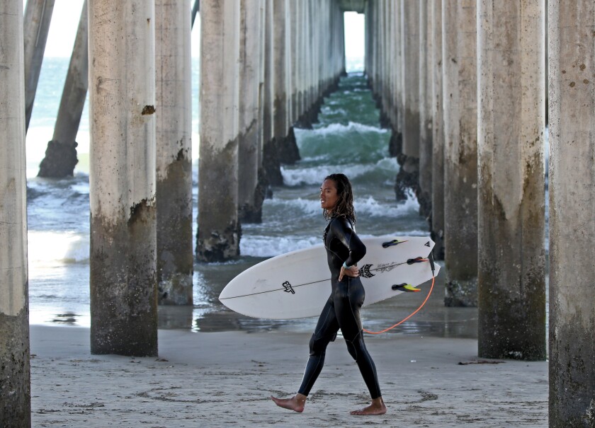 Kevin Tran walks under the pier after a day of surfing in Huntington Beach on July 31.