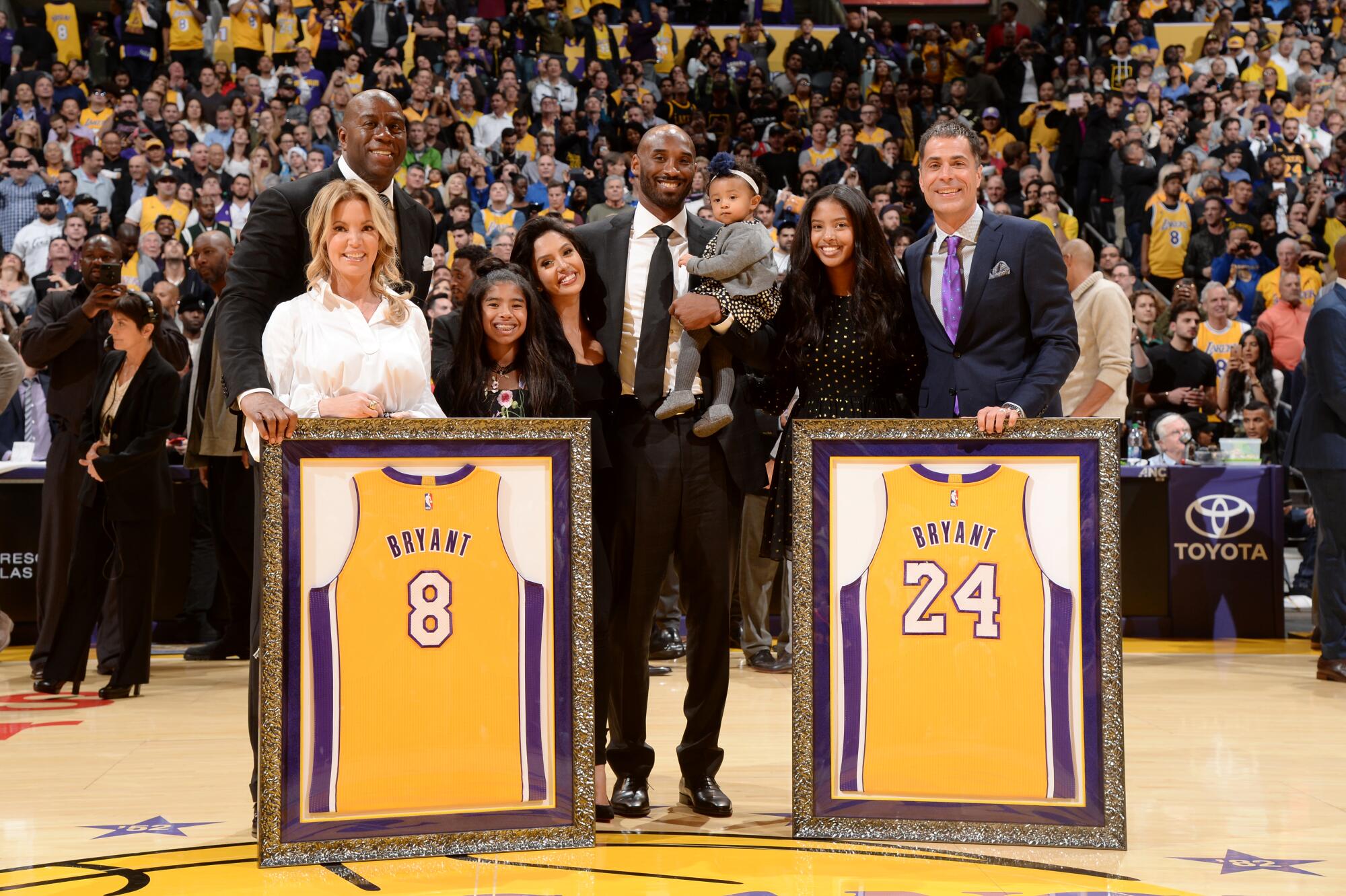 Kobe Bryant and his family pose with Magic Johnson, Jeanie Buss and Rob Pelinka during the ceremony to retire his jerseys.