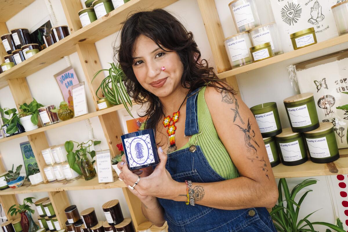 Los Angeles, CA - December 1 - Ely Valdivia, an artisan and owner of Earthy Corazon, holds a special edition pine scented candle honoring El Pino at Earthy Corazon in Los Angeles, Calif. on Dec. 1, 2023. El Pino is a pine tree located in East Los Angeles regarded as a city landmark by locals. (Carlin Stiehl / For De Los)