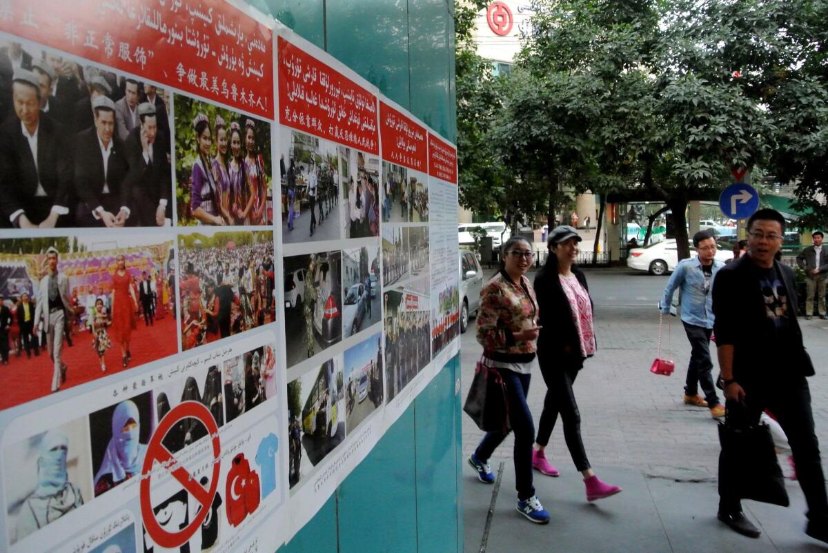Pedestrians walk past anti-terror propaganda posters pasted along the streets of Urumqi in China's Xinjiang region on Sept. 16, 2014.