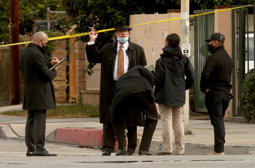 Members of the FBI talk to three people in the street near yellow police tape.