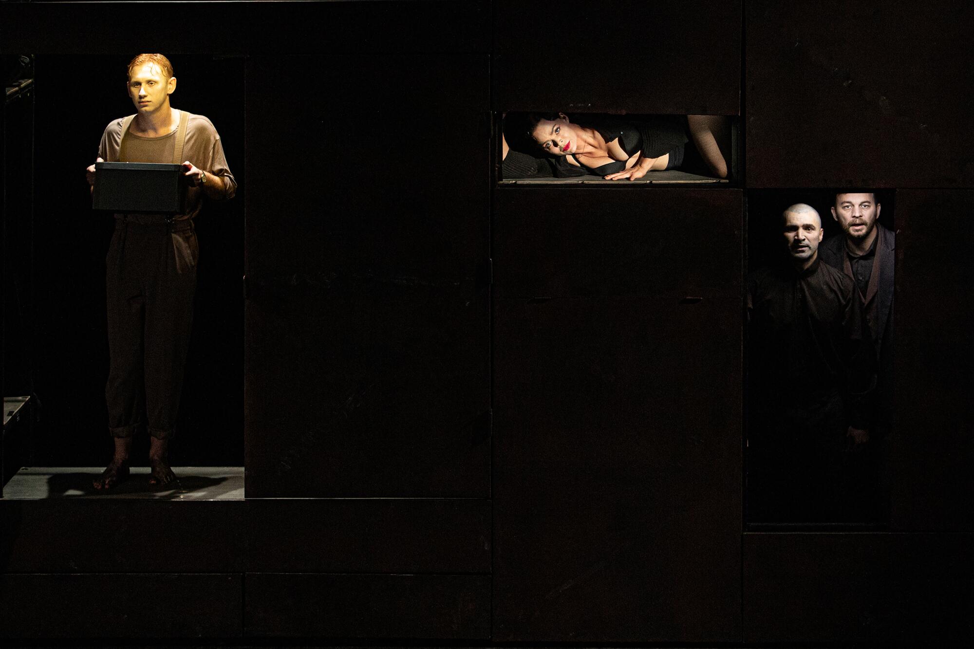 Four cast members' faces are lighted up on an otherwise dark stage