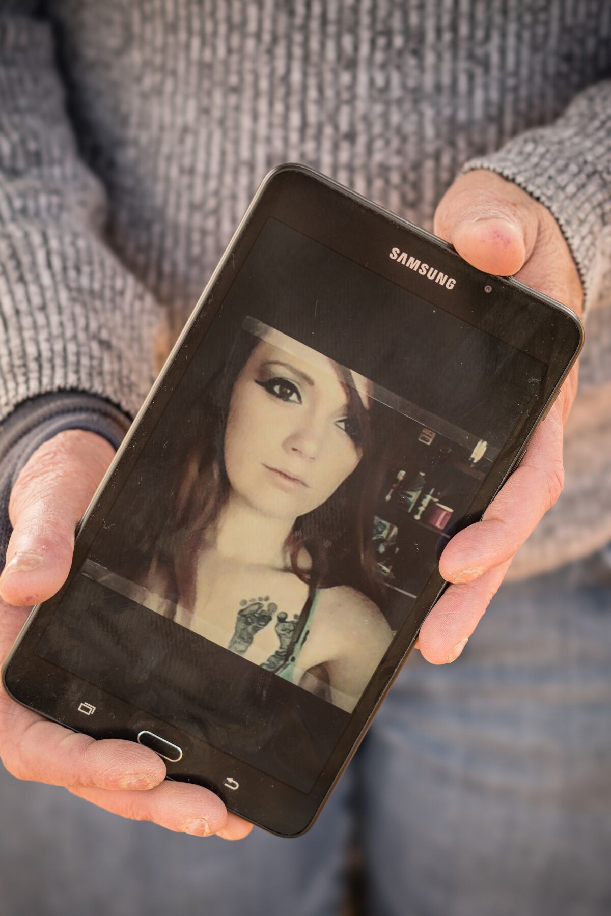 A woman's hands hold a cellphone with the image of a young woman with baby footprints tattooed on her chest.