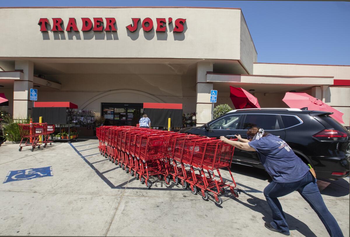 A person pushes shopping carts to a collection area outside of Trader Joe's.
