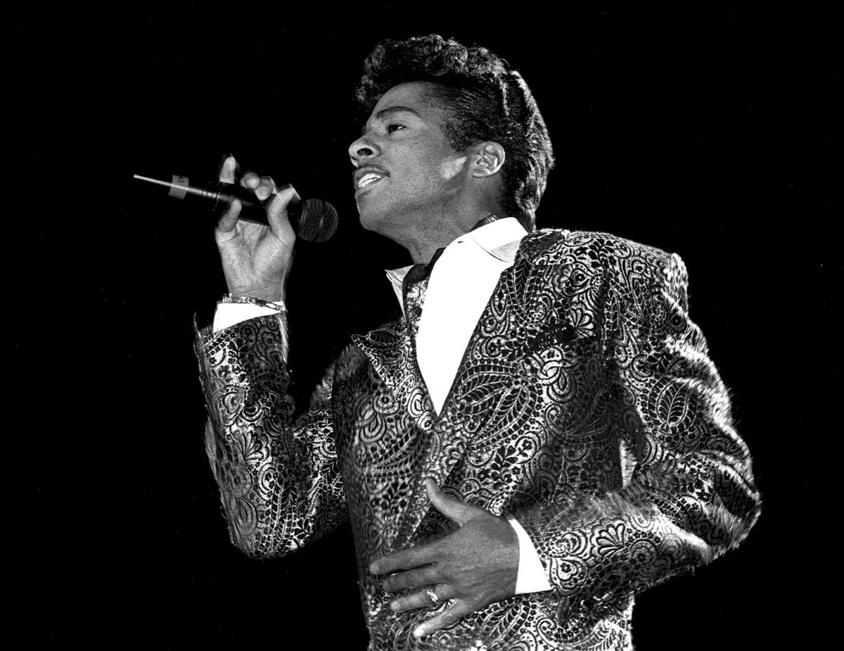 A man singing onstage wearing a brocade jacket.