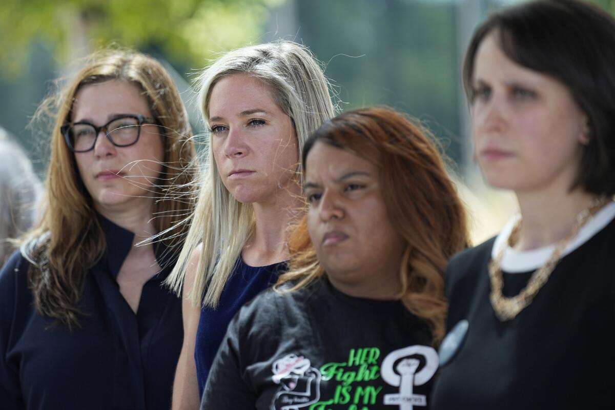 Four women stand, determined expressions, outside the Travis County Courthouse.