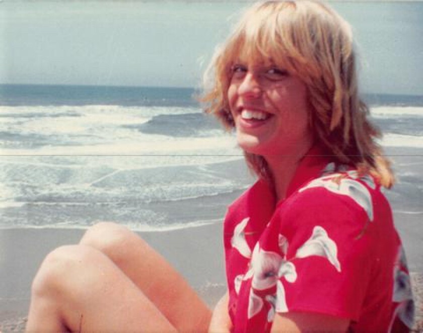 A young woman in a Hawaiian shirt smiles for a photo. In the background is a beach.