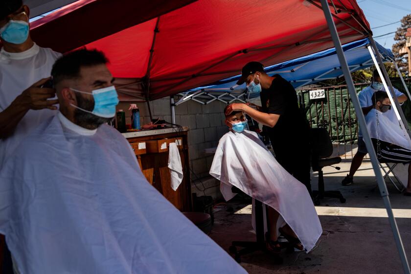 LAWNDALE, CA - SEPTEMBER 01: Nader Salameh, left and his son Gavyn,9, center, from Lawndale, get their hair cut by barbers Anthony Ho, left and Christian Mikhail, center, in the parking lot of Press Box Barber Shop, during the coronavirus pandemic, in Lawndale, CA, Tuesday, Sept. 1, 2020. The barbershop moved their work outside about one month ago, after seeing restaurants around the southbay doing the same. (Jay L. Clendenin / Los Angeles Times)
