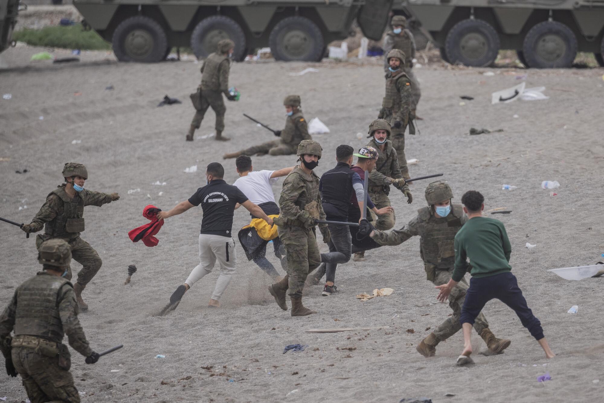 A group of soldiers fight with batons against five young male migrants on a beach