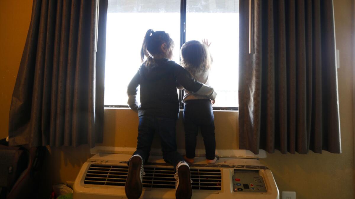 Madelyn, left, puts her arm around her little sister Mayla, as they look out the window of a motel room that is their home in North Hills.