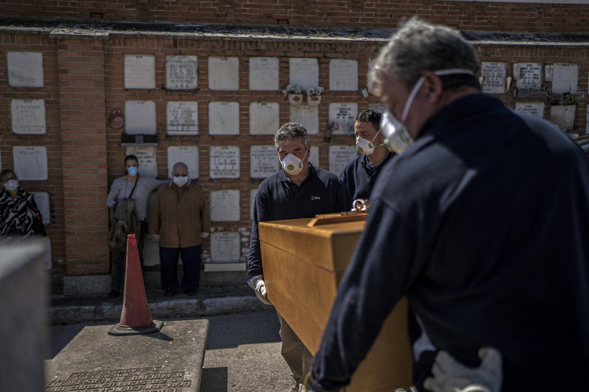 SPAIN:  Two family members watch as the coffin of an elderly COVID-19 victim is placed in a grave at the Almudena cemetery in Madrid.