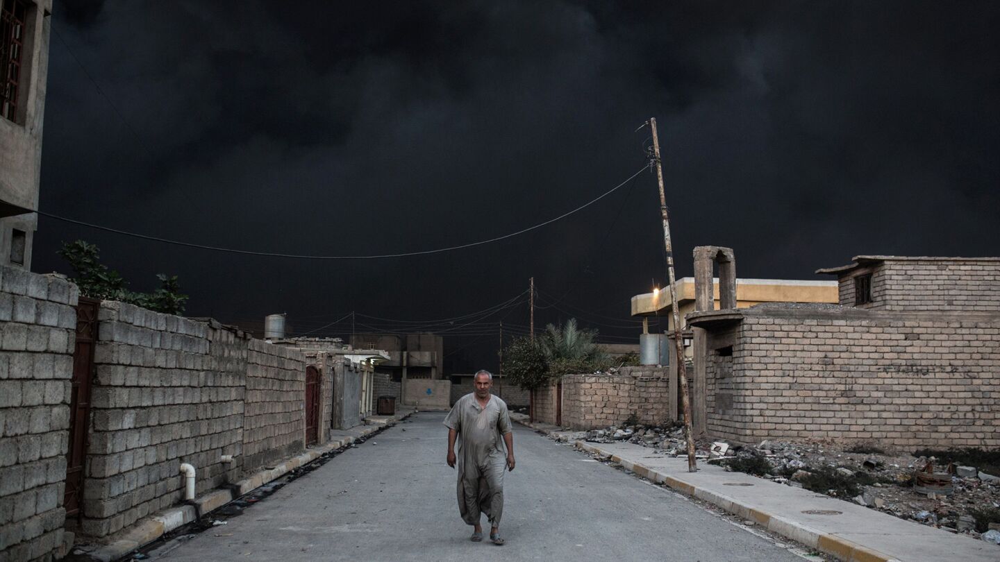 A villager walks on a bare street as smoke from oil fires nearby turn the sky black in the Qayyarah area, about 60 kilometers south of Mosul, on Oct. 19, 2016.