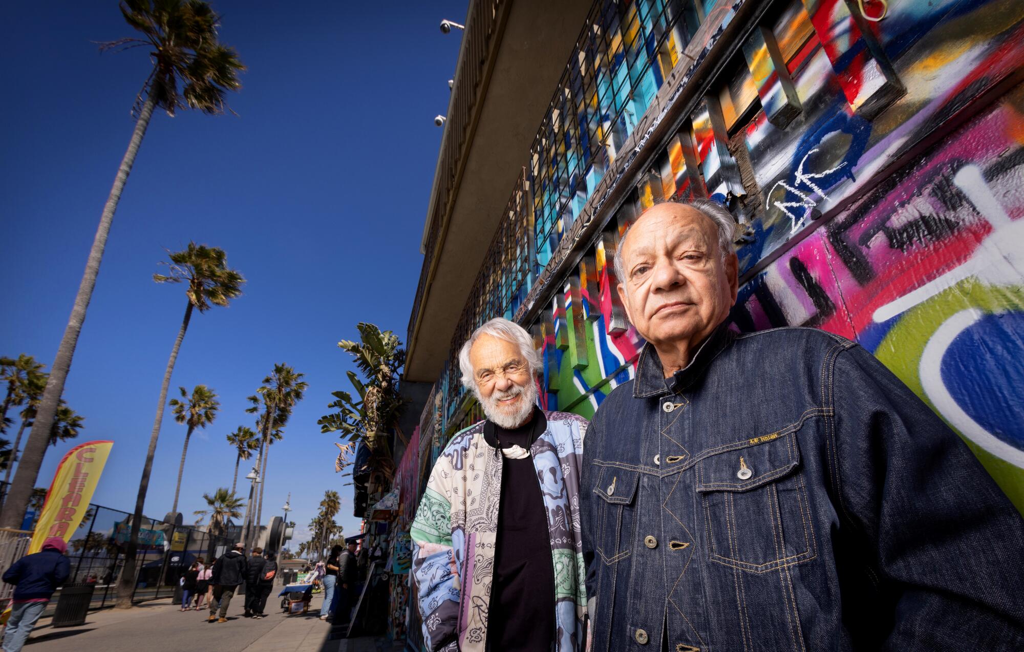 Two men pose in front of palm trees and a deep blue California sky.