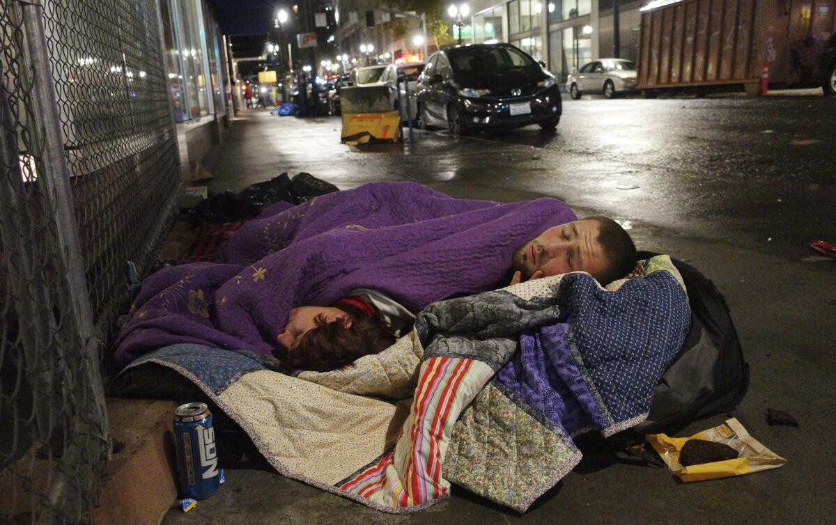 Two people sleep on a street in downtown Portland