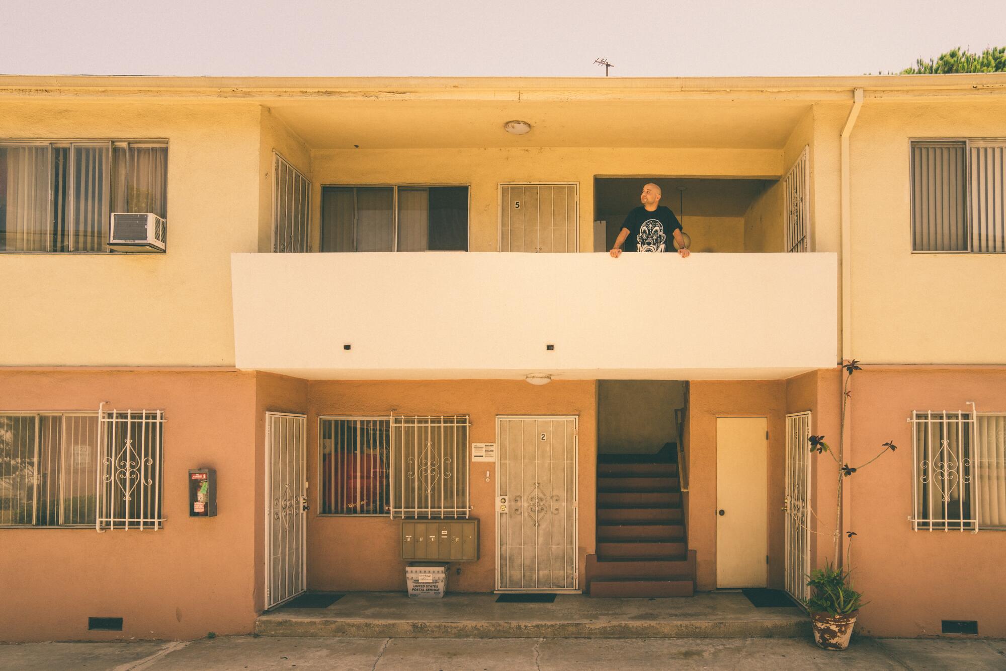 A man looks out from a balcony at an apartment complex