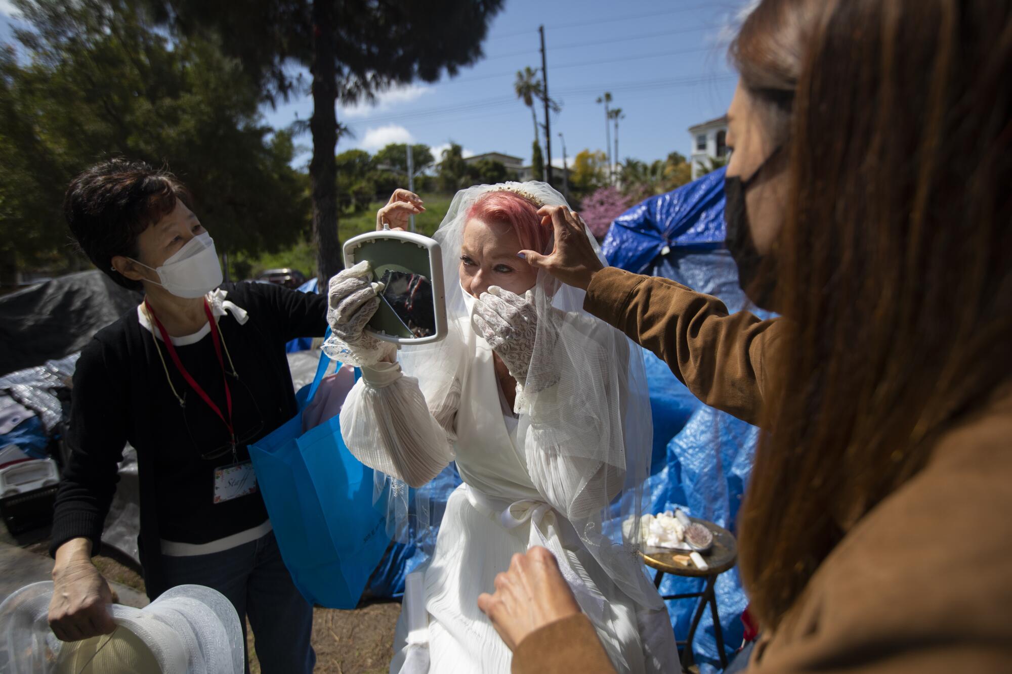 Heather Yoo, left, and Amie Roe, right, help Valerie Zeller with her wedding veil next to her tent.