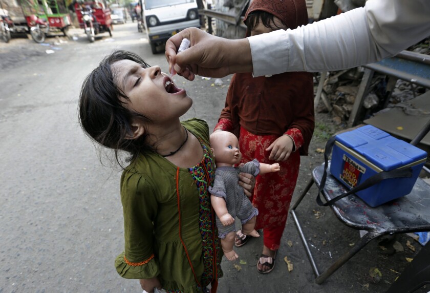 A health worker gives a polio vaccine to a girl on a street in Lahore, Pakistan, Monday, June 27, 2022. Pakistan launched a new anti-polio drive on Monday, with the goal to vaccinate a million children across Pakistan. (AP Photo/K.M. Chaudary)