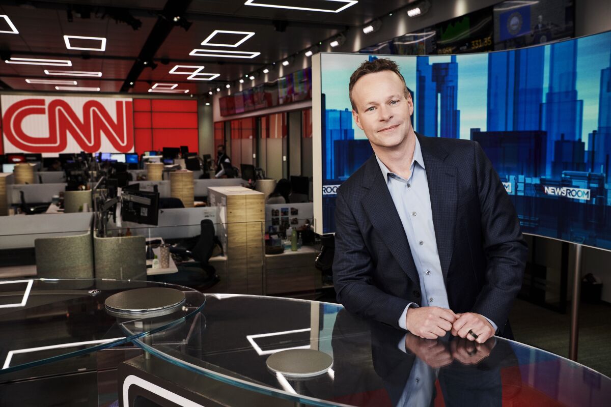 A man in a suit sits at a glass desk in the CNN newsroom.