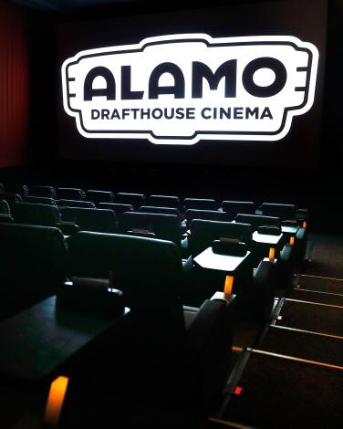A movie theater's seats face the screen, on which is projected the logo for Alamo Drafthouse Cinema.