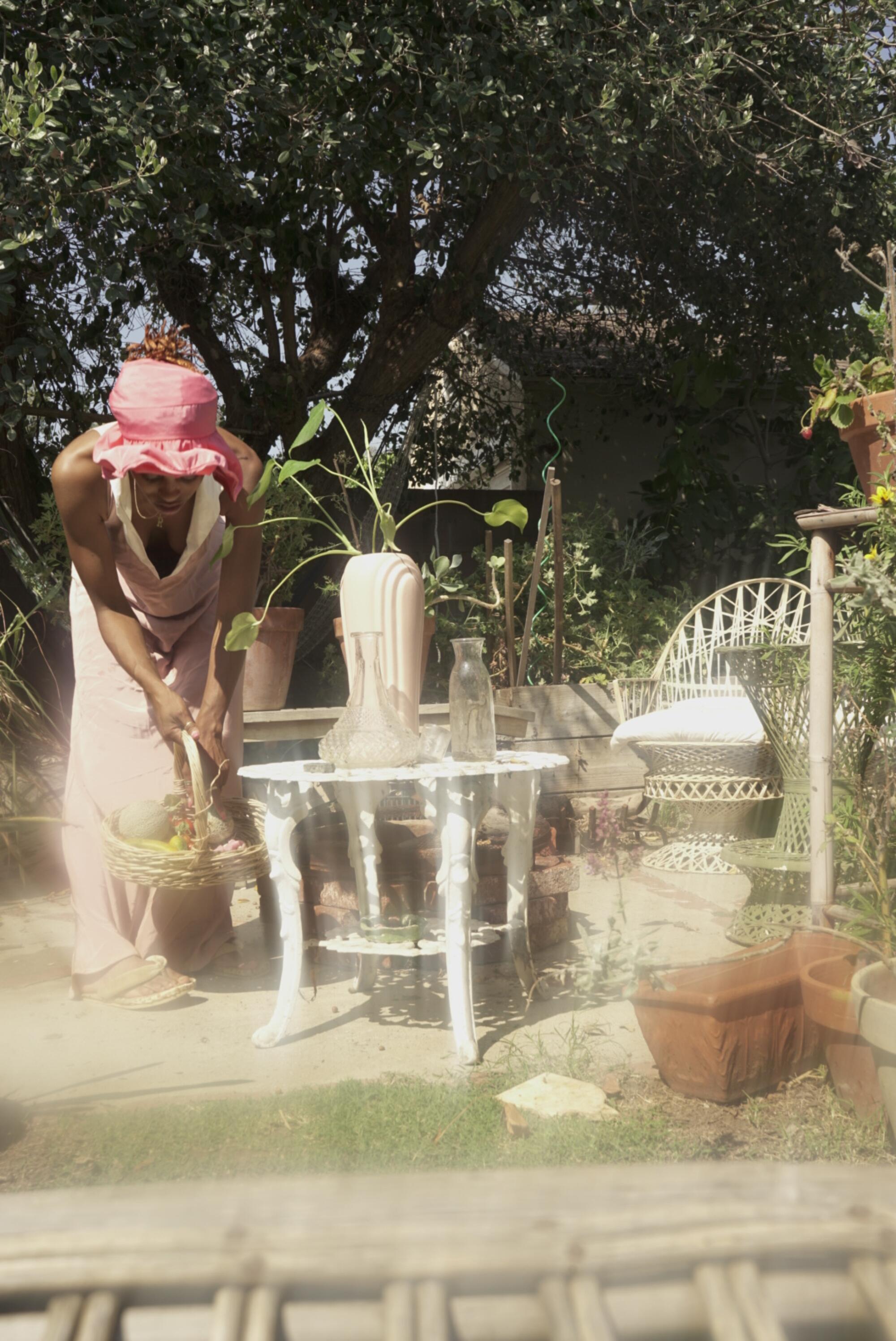A woman holding a basket tends to her garden.