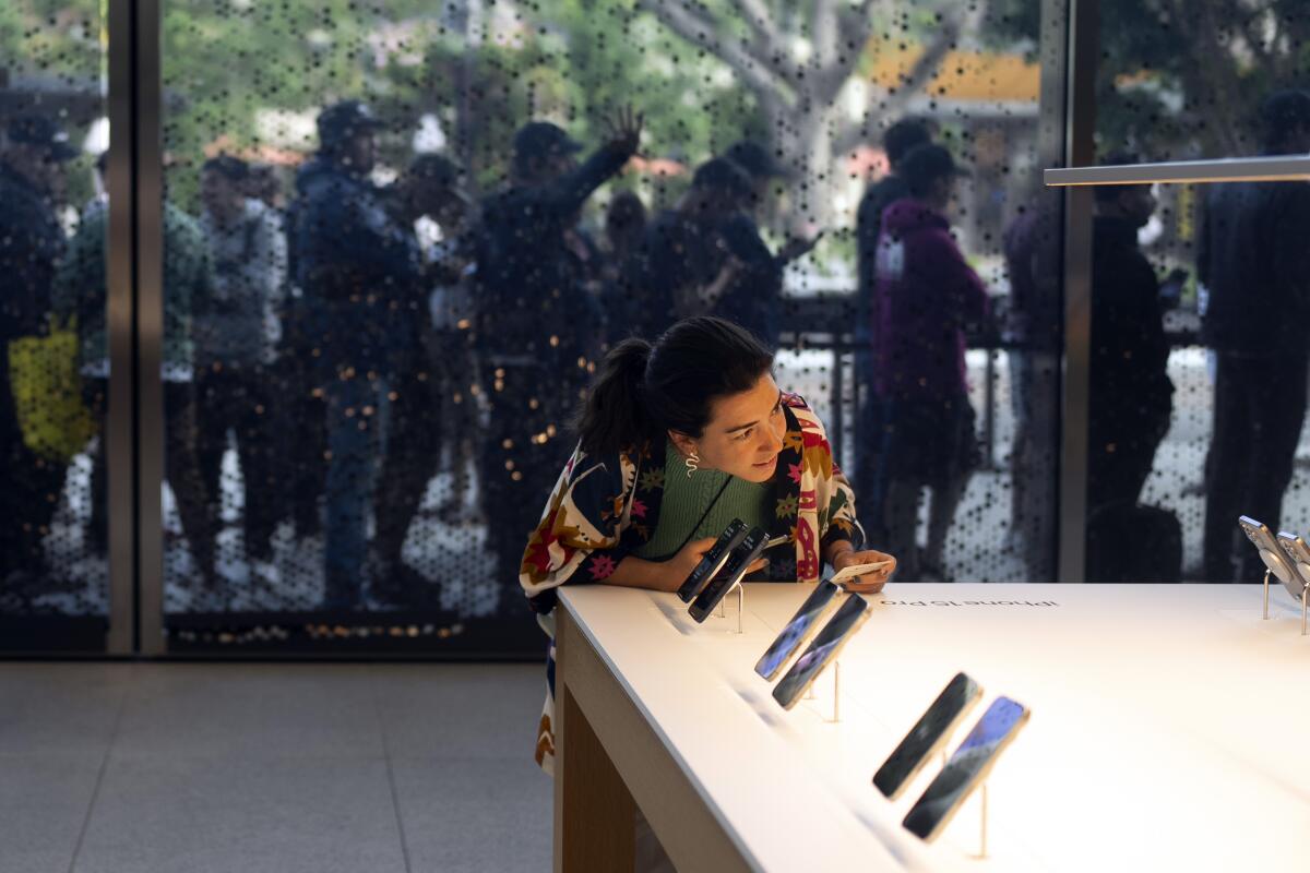 As shoppers wait in the background, a woman looks at Apple's new iPhone 15 at an Apple Store in Los Angeles