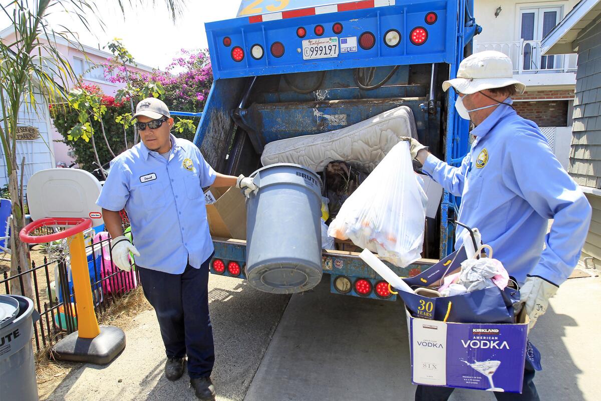 Newport Beach city trash collectors David Guzman, left, and Art Mitchell collect trash in a back alleyway, between Montero Avenue and Anade Avenue, in Newport Beach on Monday.