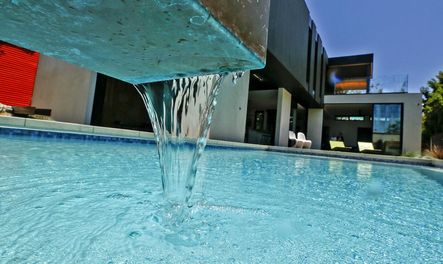 Water flows into the swimming pool through a sleek U-shaped metal channel.
