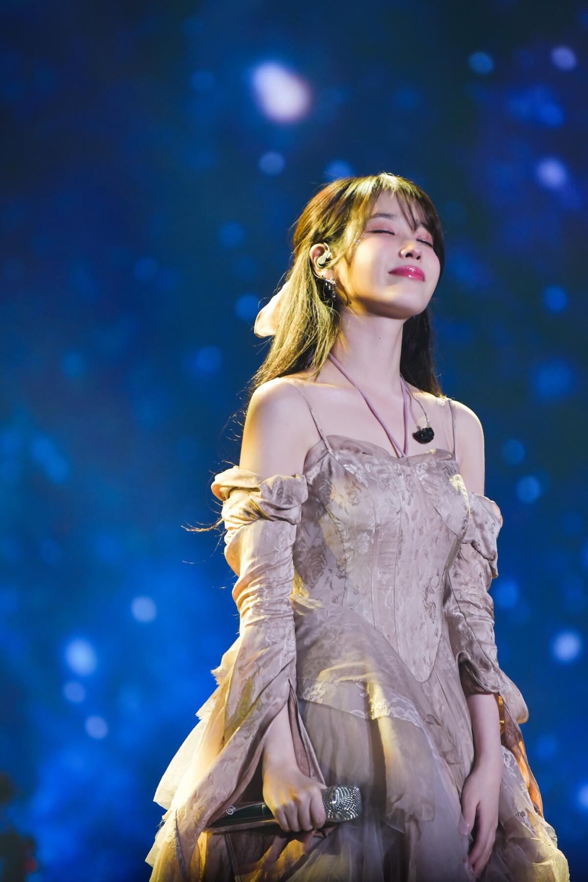 IU wears a dress and beams from the stage.
