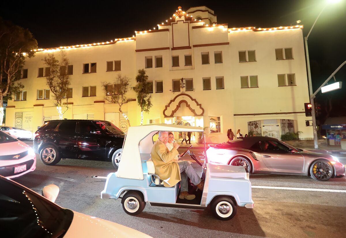 A couple in a classic covered golf cart arrive at Hospitality Night in downtown Laguna Beach on Friday.