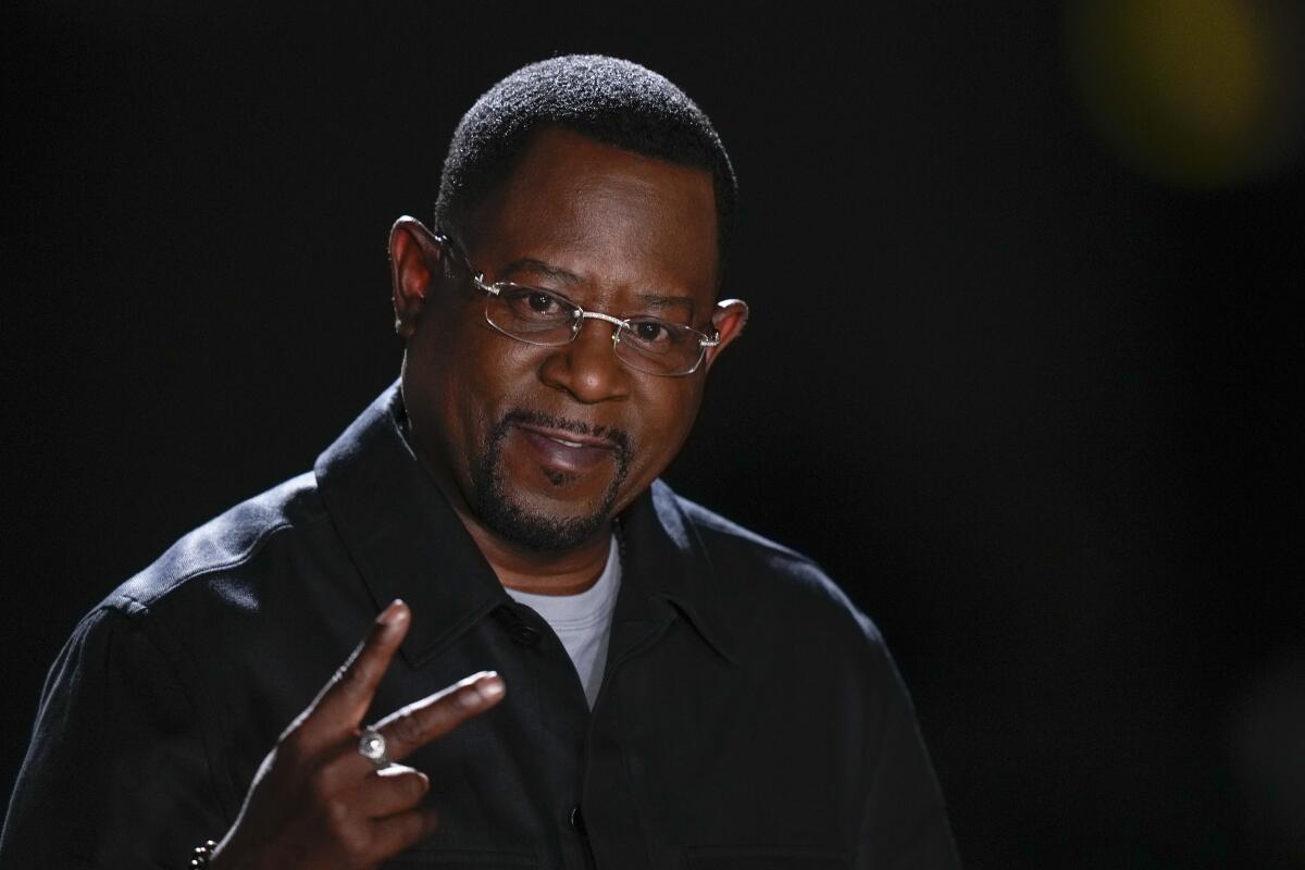 Martin Lawrence wears wire-rimmed glasses and makes the peace sign with his hand
